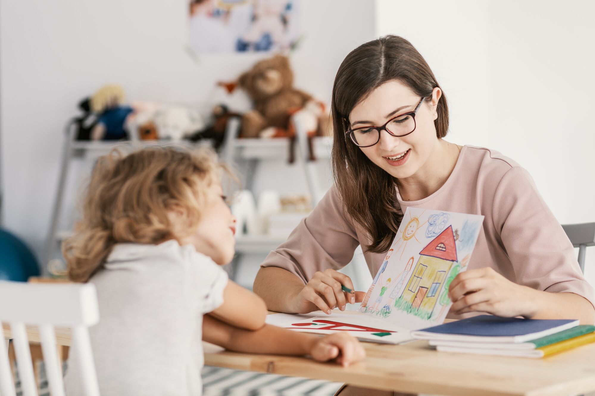 A smiling woman shows a colorful drawing to a young child, fostering creativity and interaction during a playful learning session.